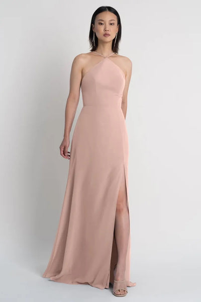 Woman in a blush pink halter neckline evening gown with a thigh-high slit, the Ingrid Bridesmaid Dress by Jenny Yoo from Bergamot Bridal.