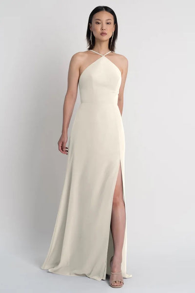 A woman in an elegant one-shoulder cream Ingrid bridesmaid dress by Jenny Yoo with a thigh-high side slit from Bergamot Bridal.