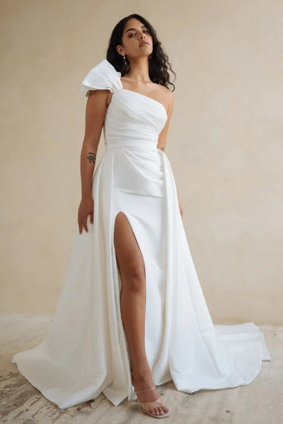 Woman posing in an elegant Isla - Jenny Yoo Wedding Dress gown with a dramatic pleated overskirt and a slit from Bergamot Bridal.
