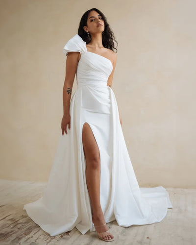 Woman in an elegant white Isla gown by Jenny Yoo Wedding Dress with a thigh-high slit, crafted from luxe taffeta, posing for a photograph.