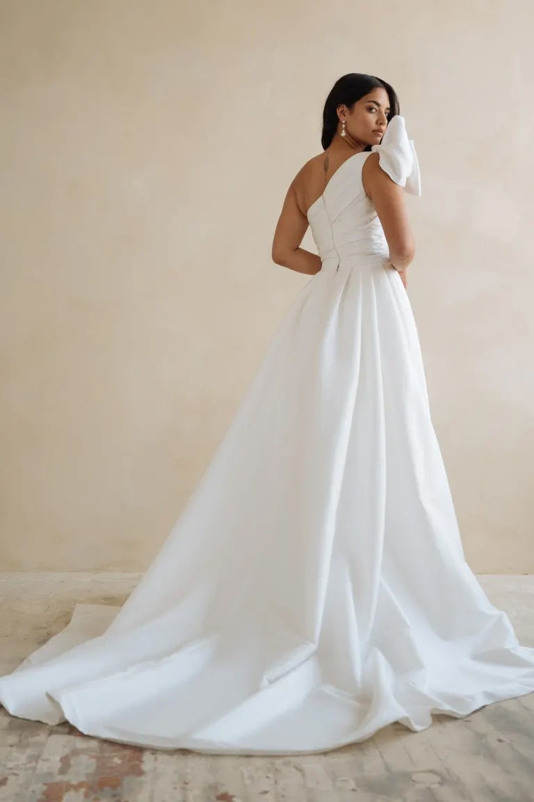 A woman in an elegant white Isla - Jenny Yoo Wedding Dress gown with a train standing against a neutral backdrop.