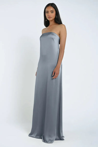 Person standing in a light grey, strapless, floor-length James Bridesmaid Dress by Jenny Yoo, crafted from luxe satin fabric, against a plain, white background.