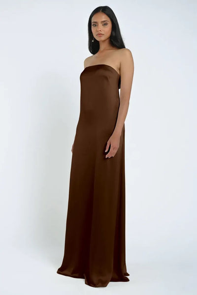 A woman stands against a plain background, donning the strapless, floor-length James Bridesmaid Dress by Jenny Yoo from Bergamot Bridal. Her hair is straight, and she wears a neutral expression.