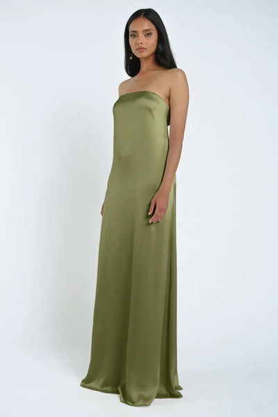 A woman dressed in a strapless, floor-length olive green James Bridesmaid Dress by Jenny Yoo from Bergamot Bridal, made of luxurious satin fabric, stands against a plain white background.