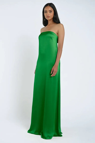 A woman stands wearing the James Bridesmaid Dress by Jenny Yoo from Bergamot Bridal, a luxurious satin fabric strapless green gown with a straight silhouette and minimal design.