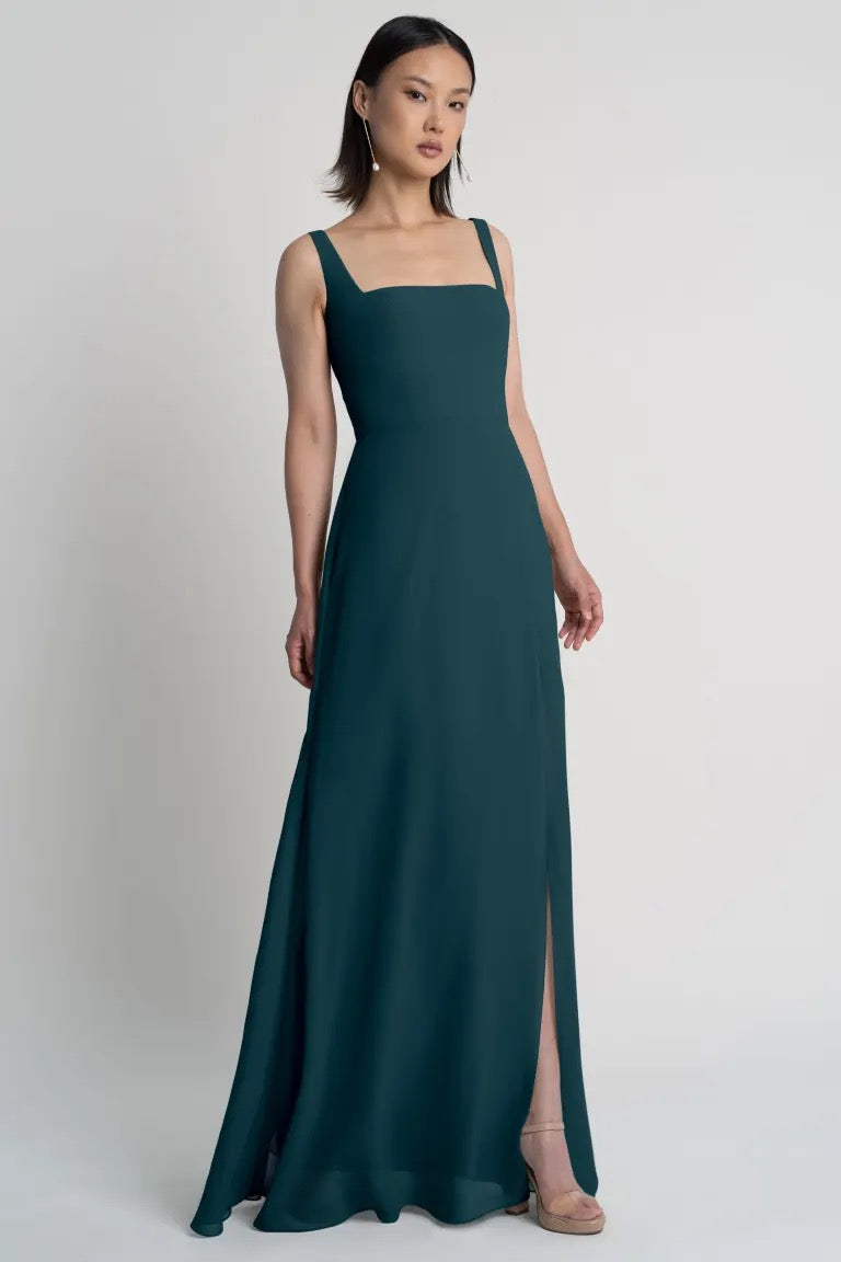 A woman poses in a sleek teal chiffon bridesmaid dress featuring an A-line skirt and a square neckline, the Jenna Bridesmaid Dress by Jenny Yoo at Bergamot Bridal.