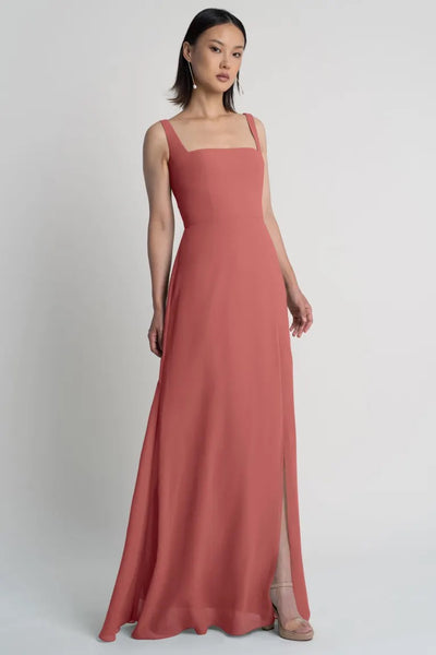 Woman in a sleek, Jenna - Bridesmaid Dress by Jenny Yoo evening gown with a side slit posing against a neutral background.