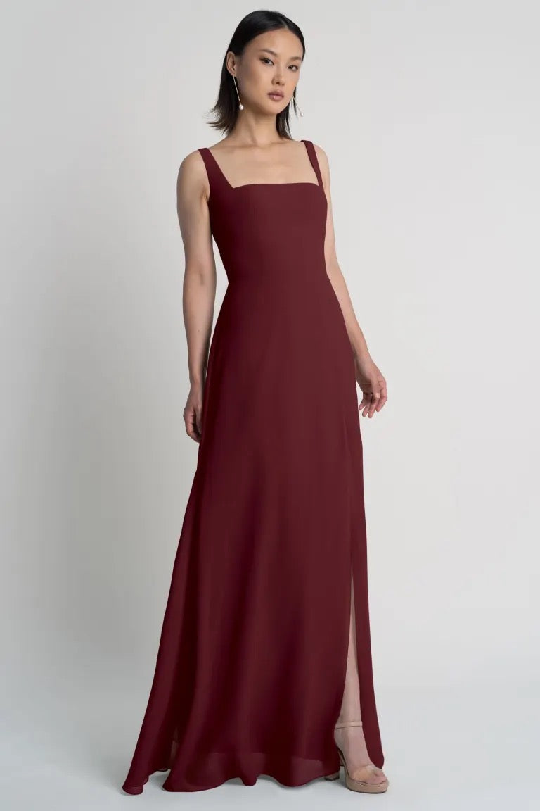 Woman modeling an elegant burgundy evening gown with a square neckline, the Jenna Bridesmaid Dress by Jenny Yoo at Bergamot Bridal.
