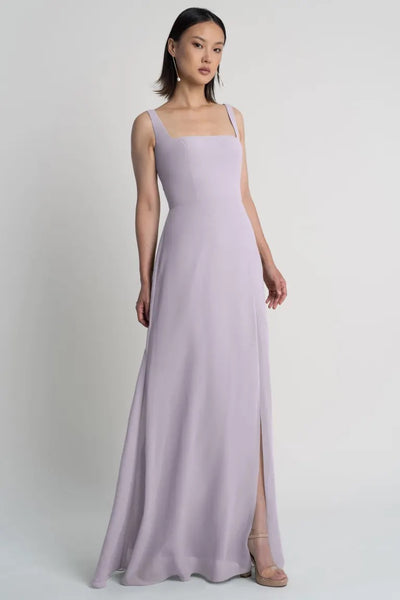 A woman posing in a light purple chiffon sleeveless evening gown with a square neckline, the Jenna Bridesmaid Dress by Jenny Yoo from Bergamot Bridal.