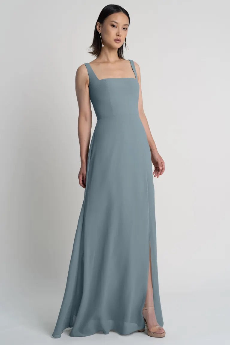 Jenna posing in a simple grey chiffon bridesmaid dress with a square neckline and a subtle side slit, the Jenna - Bridesmaid Dress by Jenny Yoo from Bergamot Bridal.
