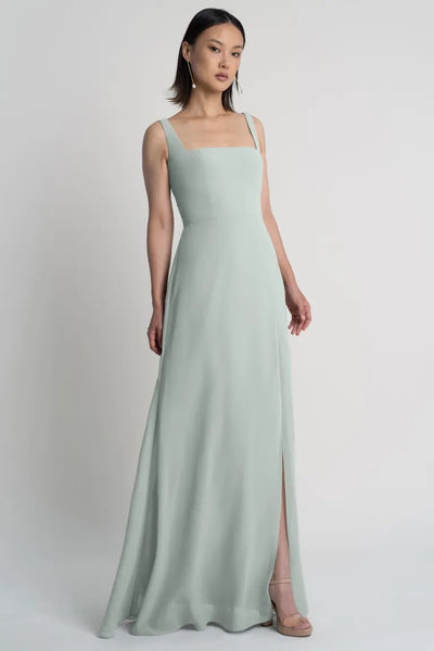 A woman modeling a long, pastel green A-line skirt evening gown with shoulder straps and a square neckline, Jenna - Bridesmaid Dress by Jenny Yoo from Bergamot Bridal.
