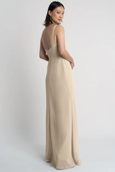 Woman posing in an elegant beige evening gown featuring a square neckline with a simple design from the back, the Jenna Bridesmaid Dress by Jenny Yoo from Bergamot Bridal.