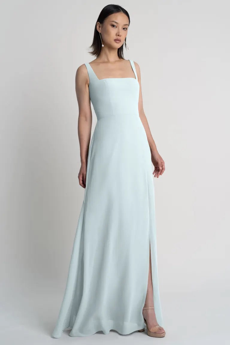 A woman modeling a Jenna Bridesmaid Dress by Jenny Yoo in light blue, floor-length evening dress with shoulder straps and a square neckline from Bergamot Bridal.