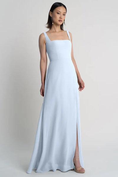 Woman posing in a simple Jenna chiffon bridesmaid dress with a side slit, against a neutral backdrop by Bergamot Bridal.