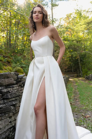 Woman posing outdoors in a white bridal gown with a leg slit, the Mollie - Jenny Yoo Wedding Dress from Bergamot Bridal.