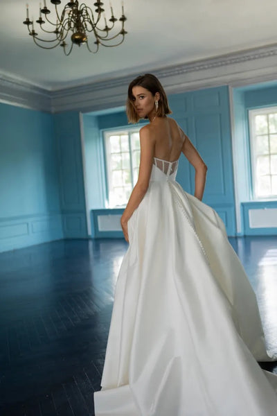 A woman in an elegant Mollie - Jenny Yoo bridal gown from Bergamot Bridal standing in a room with blue walls and wooden flooring.