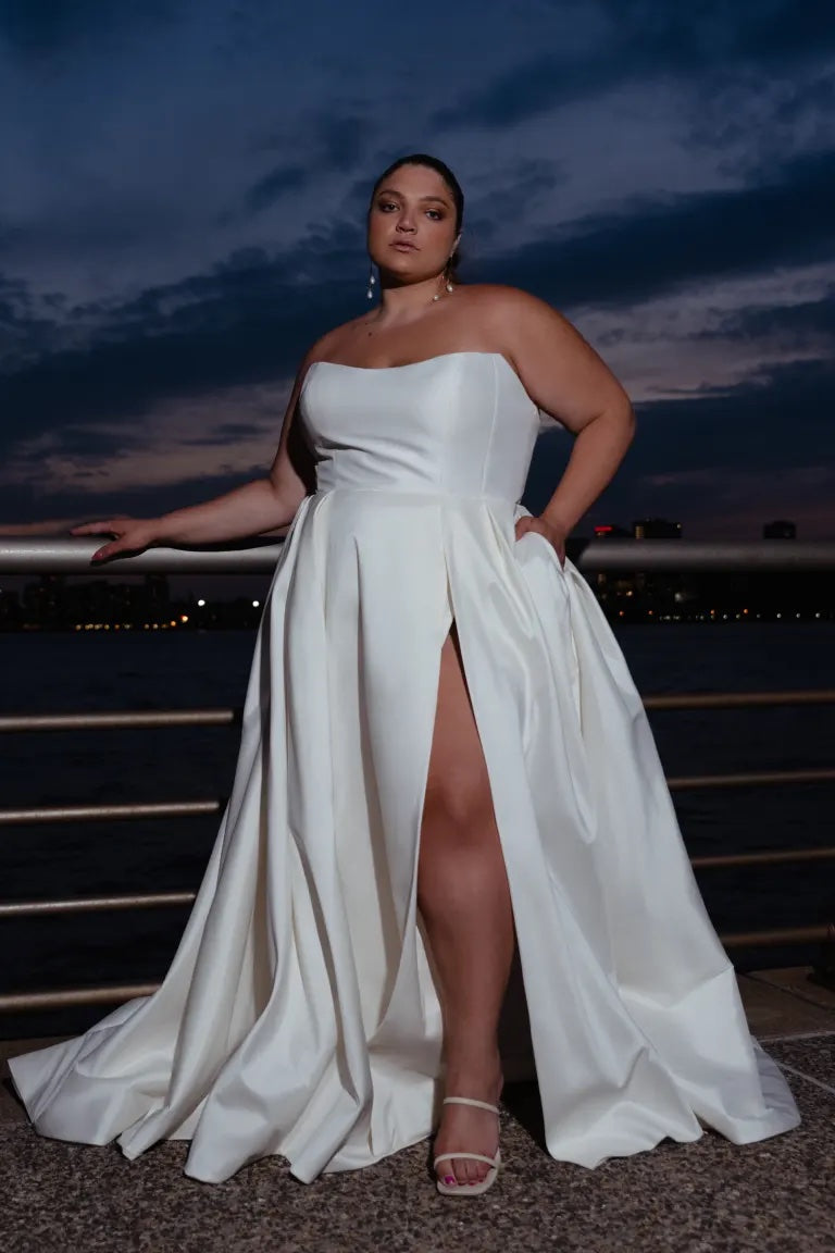 Woman in an elegant Mollie - Jenny Yoo wedding dress with an A-line skirt posing outdoors at dusk from Bergamot Bridal.