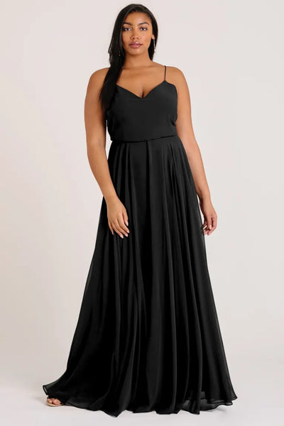 A woman in a black V-neck evening gown, designed in the universally flattering style of an Inesse chiffon bridesmaid dress by Jenny Yoo, posing for the camera.