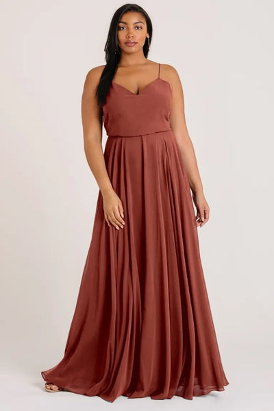 Woman wearing a flowy terracotta Inesse chiffon evening gown with a V-neck by Bergamot Bridal.