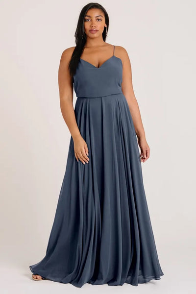 Woman posing in a sleeveless blue evening gown with a V-neck, the Inesse bridesmaid dress by Jenny Yoo from Bergamot Bridal.