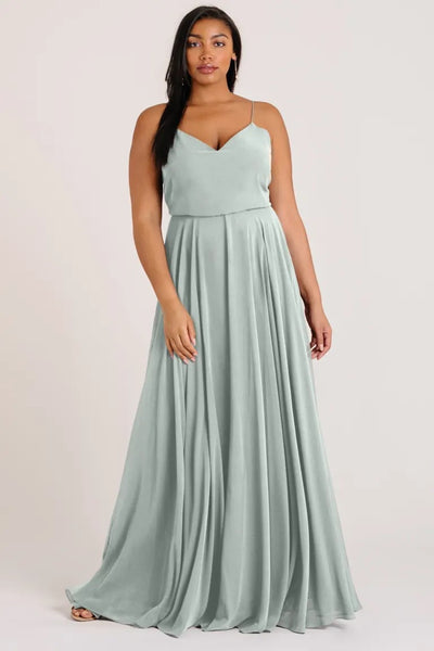 A woman wearing an elegant, Inesse chiffon bridesmaid dress by Jenny Yoo with a sleeveless V-neck top and flowing circle skirt in light green from Bergamot Bridal.