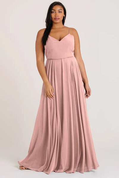 Woman in a pink Inesse - Bridesmaid Dress by Jenny Yoo with spaghetti straps, standing against a neutral background from Bergamot Bridal.