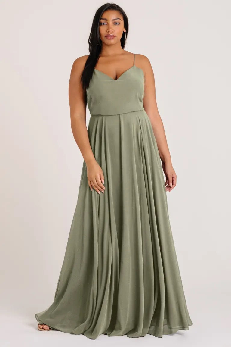 A woman modeling a Jenny Yoo Inesse chiffon, sleeveless, olive green maxi dress with a flowing skirt from Bergamot Bridal.
