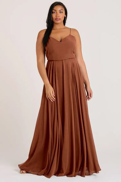 Woman in a flowing brown Inesse - Bridesmaid Dress by Jenny Yoo chiffon maxi dress standing against a neutral background from Bergamot Bridal.