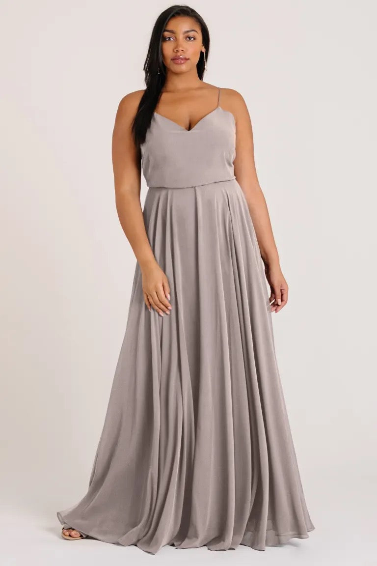 A woman modeling a flowing, gray Inesse chiffon bridesmaid dress by Jenny Yoo with a V-neckline from Bergamot Bridal.