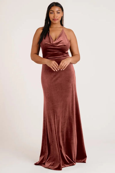A woman posing in an elegant Sullivan - Bridesmaid Dress by Jenny Yoo velvet rose sleeveless evening gown with a halter cowl neckline from Bergamot Bridal.