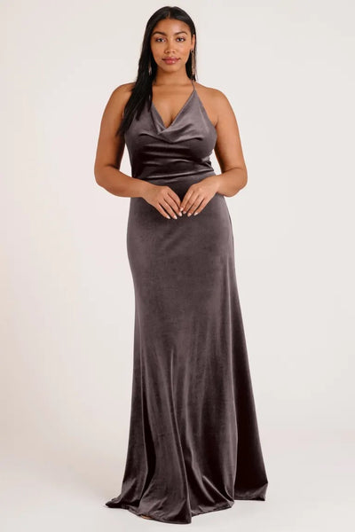 A woman in an elegant brown velvet Sullivan bridesmaid dress by Jenny Yoo with a halter cowl neckline posing against a neutral background. (Brand name: Bergamot Bridal)