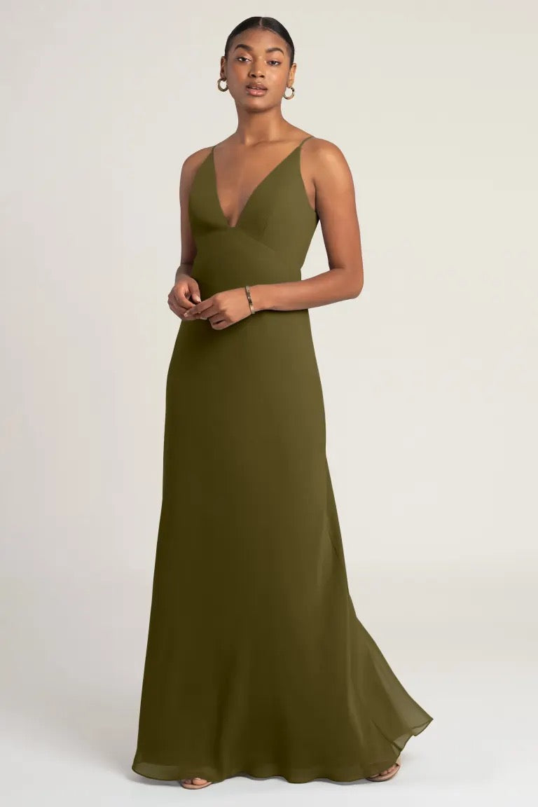 Woman in a Jude - Bridesmaid Dress by Jenny Yoo from Bergamot Bridal, an empire waist olive green evening gown posing against a neutral background.