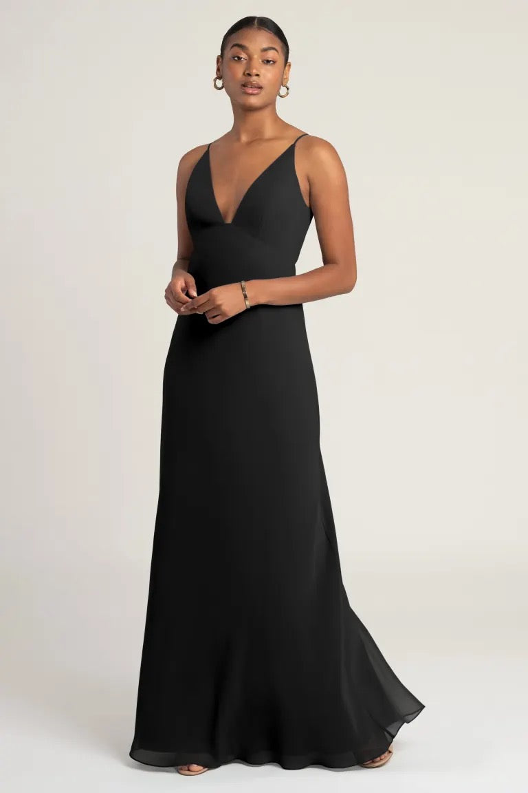 Woman in an elegant black empire waist evening gown posing against a neutral background, wearing the Jude Bridesmaid Dress by Jenny Yoo from Bergamot Bridal.