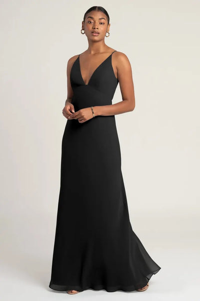 Woman in an elegant black empire waist evening gown posing against a neutral background, wearing the Jude Bridesmaid Dress by Jenny Yoo from Bergamot Bridal.