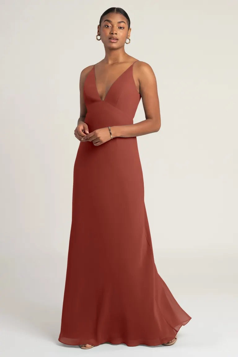Woman in an elegant rust-colored evening gown with an empire waist, the Jude - Bridesmaid Dress by Jenny Yoo at Bergamot Bridal.