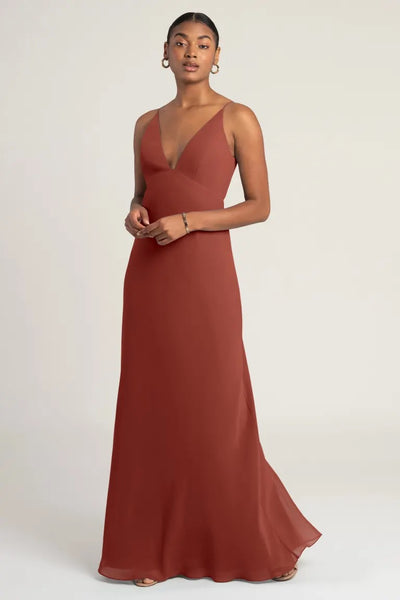 Woman in an elegant rust-colored evening gown with an empire waist, the Jude - Bridesmaid Dress by Jenny Yoo at Bergamot Bridal.