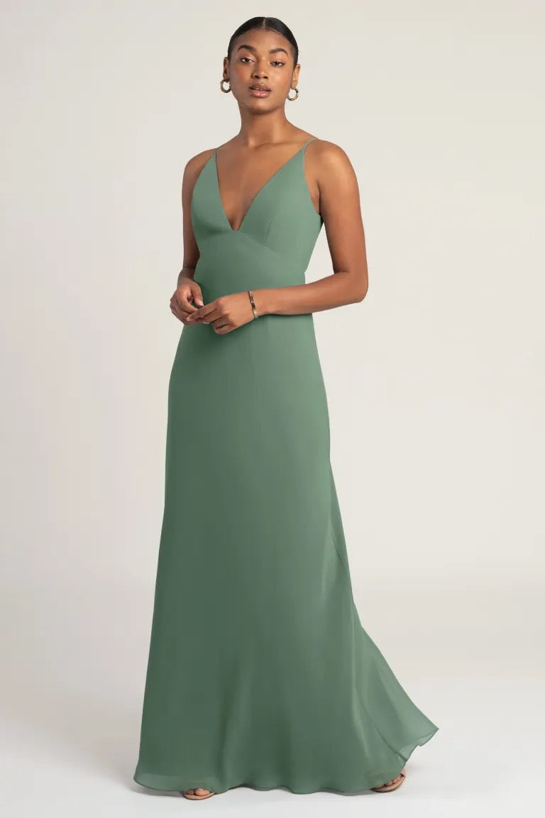 A woman models the Jude bridesmaid dress by Jenny Yoo, a formal green gown with a notched neckline and spaghetti straps, from Bergamot Bridal.