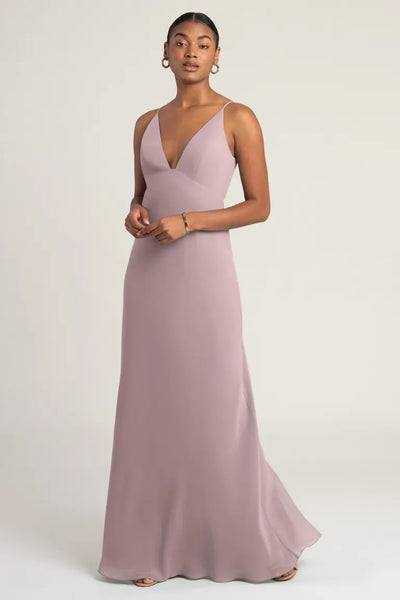 A woman wearing an elegant pink Jude Bridesmaid Dress by Jenny Yoo gown with an empire waist and a subtle flare at the bottom from Bergamot Bridal.