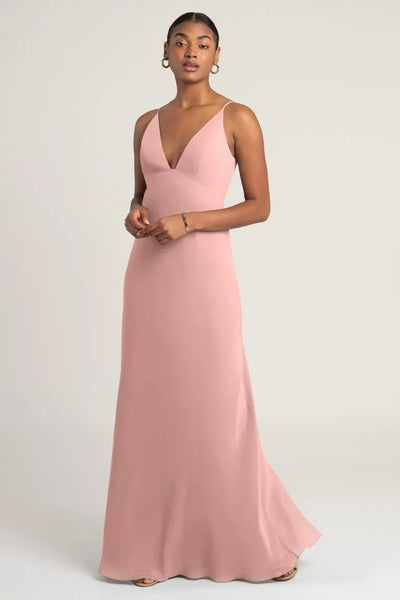 A woman posing in an elegant, blush-colored evening gown with an empire waist, the Jude Bridesmaid Dress by Jenny Yoo from Bergamot Bridal.