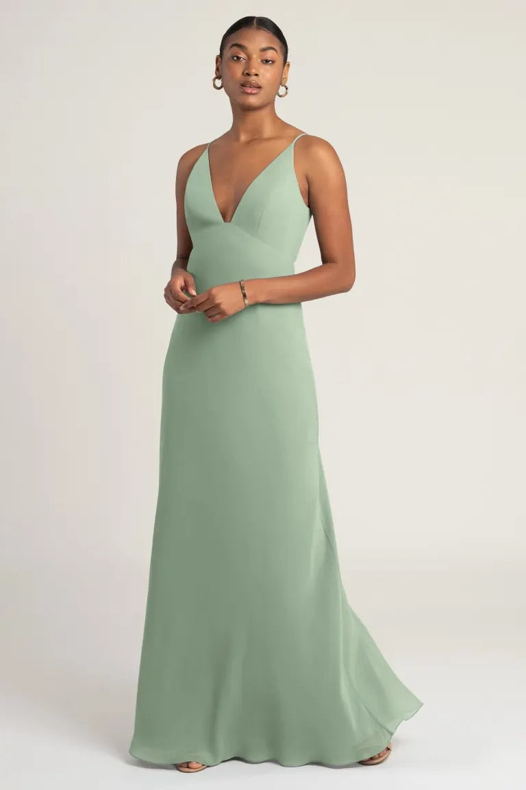 Woman in an elegant sage green chiffon Jude bridesmaid dress by Jenny Yoo with empire waist, posing for the camera from Bergamot Bridal.