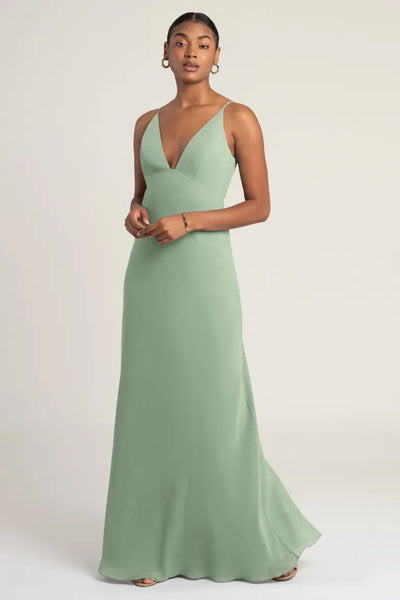 Woman in an elegant sage green chiffon Jude bridesmaid dress by Jenny Yoo with empire waist, posing for the camera from Bergamot Bridal.