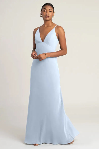 A woman wearing a light blue chiffon evening gown with an empire waist, Jude - Bridesmaid Dress by Jenny Yoo, standing against a neutral background from Bergamot Bridal.
