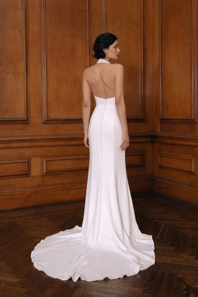 A woman stands with her back to the camera wearing an elegant white Jenny Yoo Wedding Dress gown with a buttoned trail detail and a slight train from Bergamot Bridal.