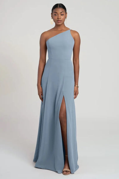 A woman modeling a light blue one-shoulder chiffon Kora - Jenny Yoo bridesmaid dress with a flattering fit and flare silhouette from Bergamot Bridal.