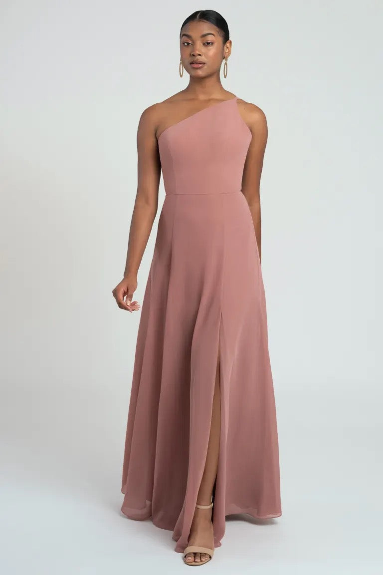 A woman in a pink one-shoulder Kora - Jenny Yoo bridesmaid dress by Bergamot Bridal posing against a white background.