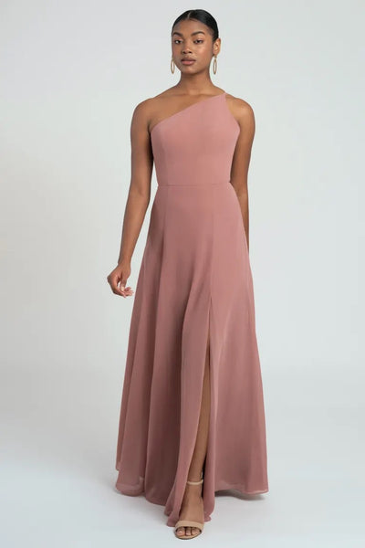 A woman in a pink one-shoulder Kora - Jenny Yoo bridesmaid dress by Bergamot Bridal posing against a white background.