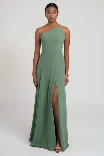 Woman posing in an elegant one-shoulder chiffon Kora - Jenny Yoo bridesmaid dress by Bergamot Bridal with a thigh-high slit, offering a flattering fit and flare silhouette for a modern look.