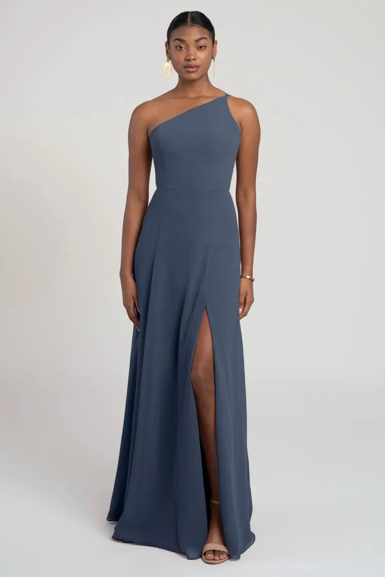 A woman wearing a Kora - Jenny Yoo bridesmaid dress in slate blue with a thigh-high slit, featuring a flattering fit and flare silhouette for a modern look from Bergamot Bridal.