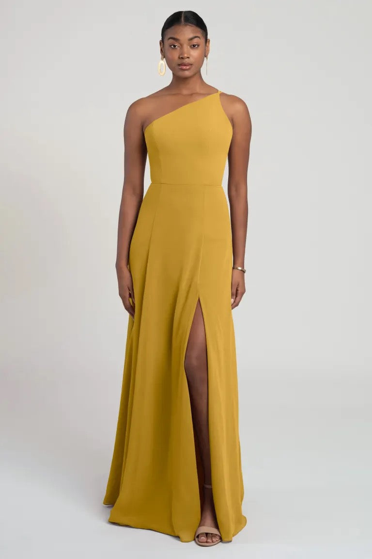 A woman in a modern look, Kora - Jenny Yoo mustard one-shoulder chiffon bridesmaid dress with a flattering fit and flare silhouette from Bergamot Bridal.