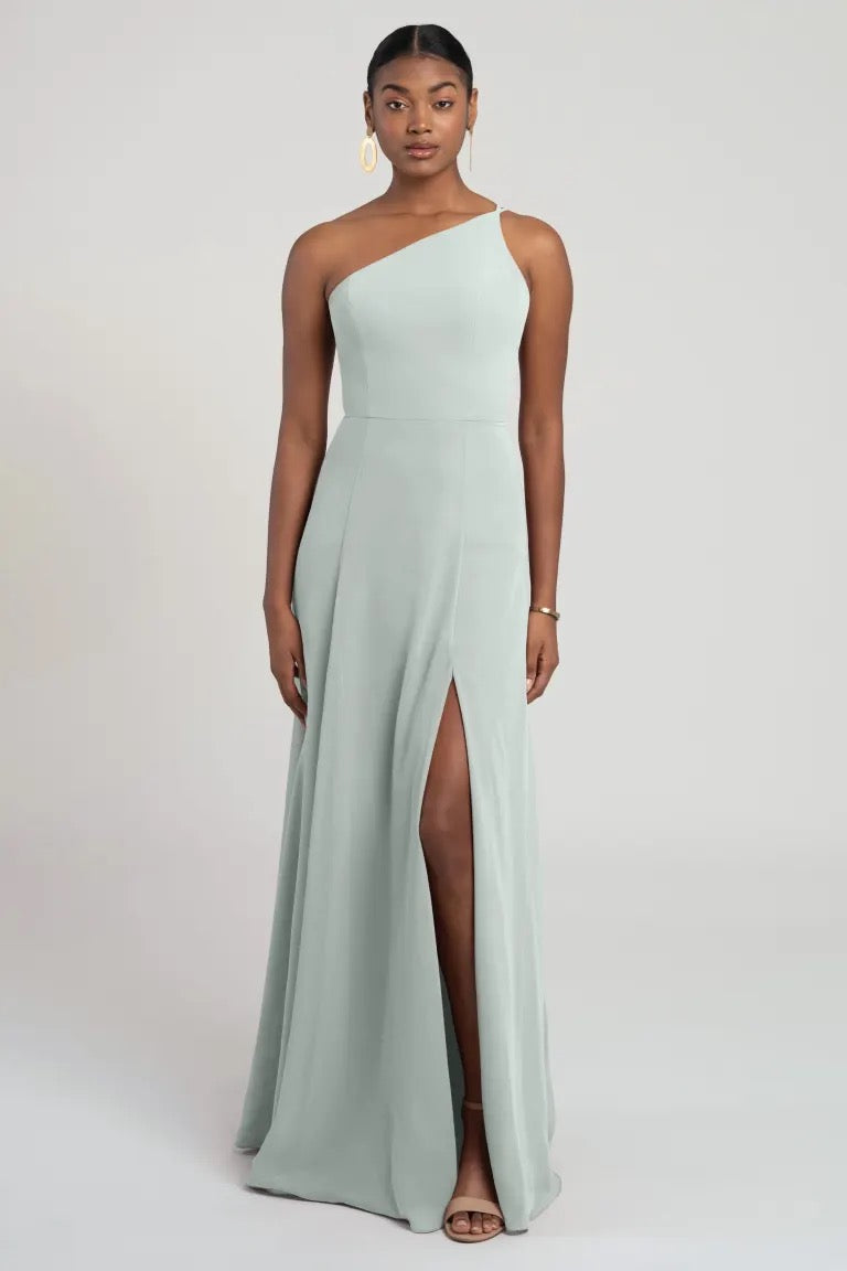 A woman posing in a Kora - Jenny Yoo bridesmaid dress, seafoam green with a thigh-high slit, flaunting a flattering fit and flare silhouette by Bergamot Bridal.